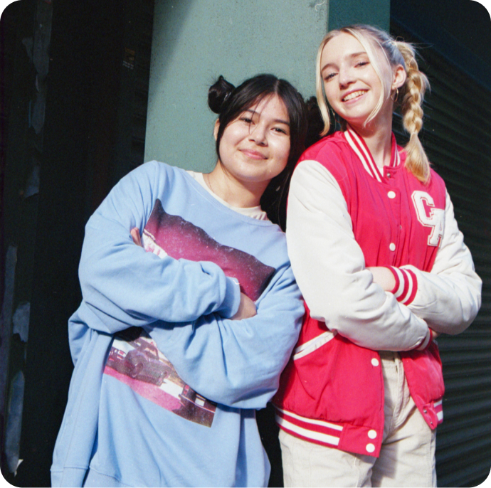 two girls crossing their arms and leaning on eachother, smiling